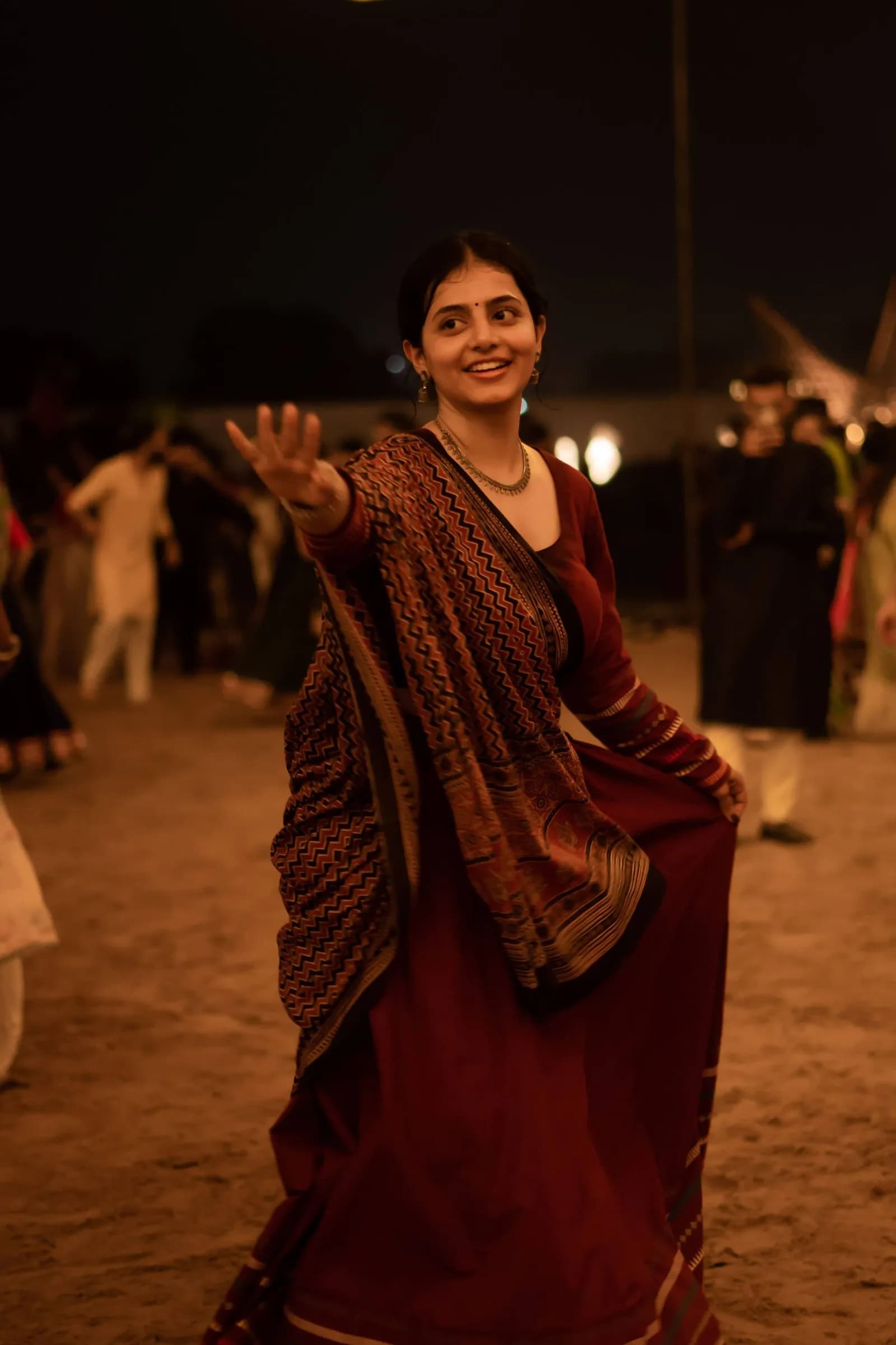 A dancer in a dark sari on the sand, lit from behind