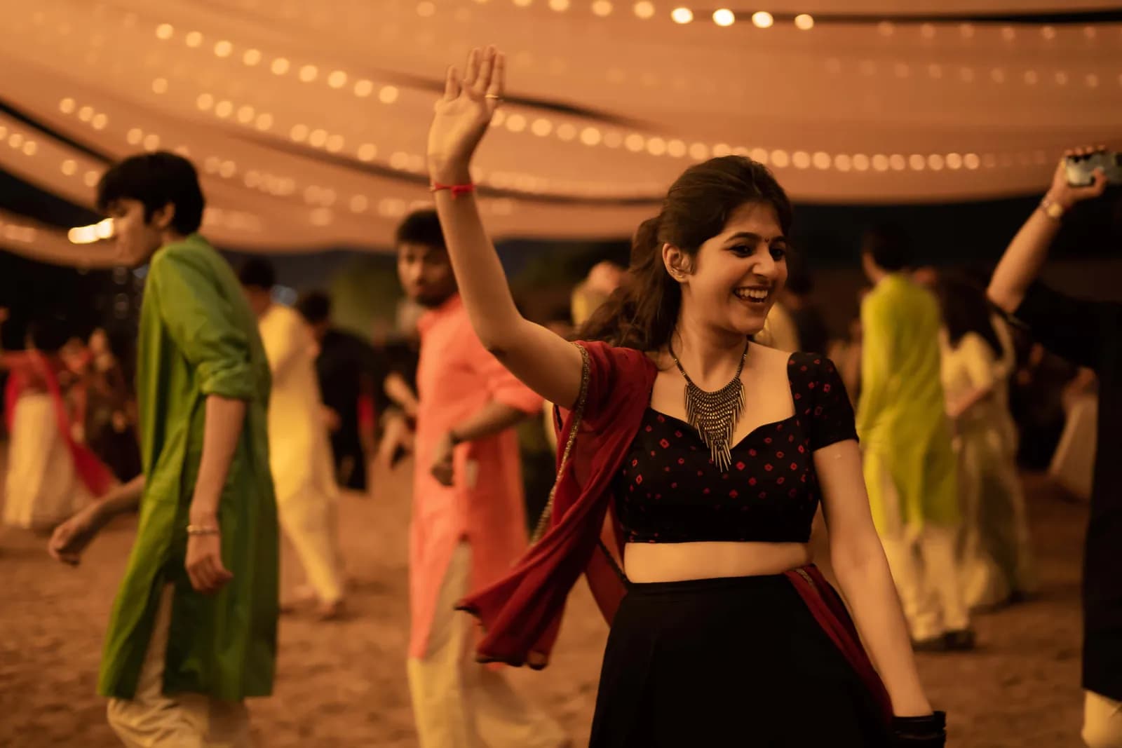 A circle of dancers in bright chaniya cholis under a canopy of lights