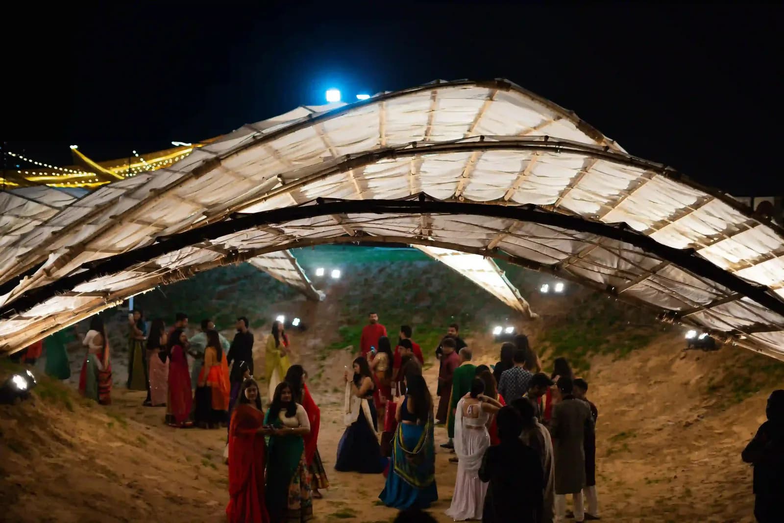 A lit fabric canopy over a garba ground with a crowd gathering beneath it